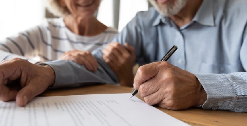 Close up of 60s husband and wife sit at desk sign health insurance contract close deal, smiling old mature couple spouses put signature on document make good agreement, elderly healthcare concept